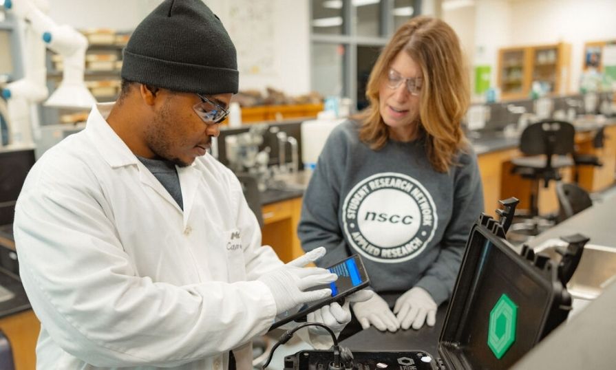 A student researcher talking to Student Research Network coordinator in a lab while working. 