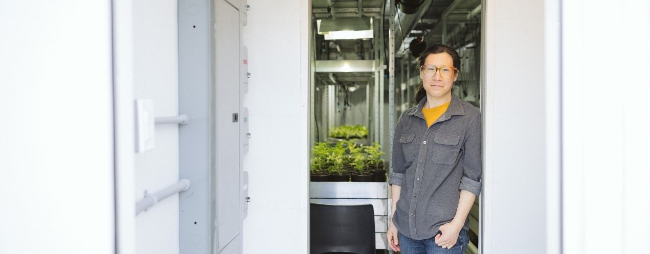 Person standing outside a controlled grow space with plants visible inside.