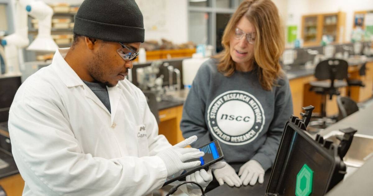 A student researcher and colleague examine laboratory equipment together.