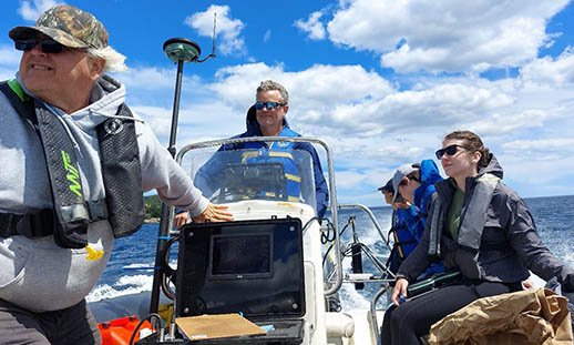 Five people travelling in a Zodiac boat on the ocean with wind blowing in their hair and blue cloudy skies in the background.  