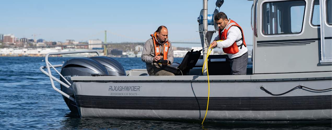 Two researchers deploying a piece of equipment off the side of a research boat.