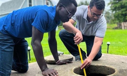 wo men inspecting a well, using equipment to measure water quality or levels.