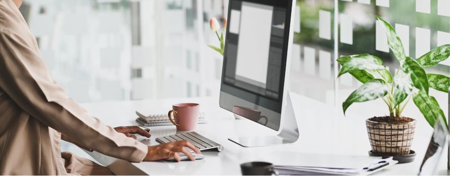 Woman typing on a computer in a clean workspace beside a plant