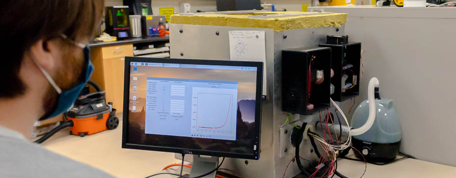 Researcher in a lab looking at data on a computer connected to an environmentally controlled chamber.