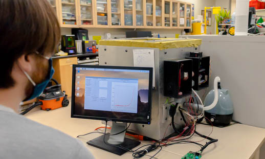 Researcher in a lab looking at data on a computer connected to an environmentally controlled chamber.