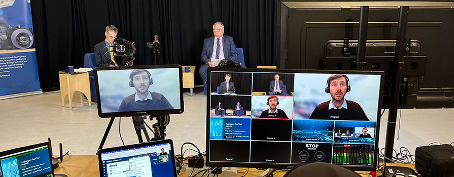 Technical event setup, showing virtual speaker on monitor and two in person presenters. 