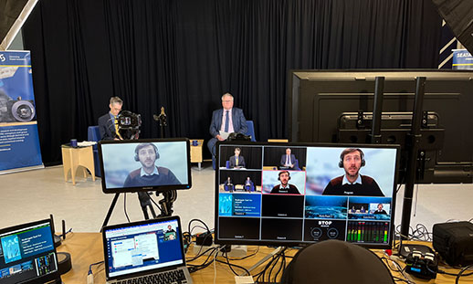 Technical event setup, showing virtual speaker on monitor and two in person presenters. 