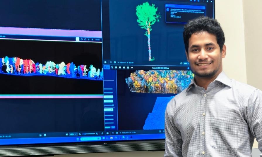  A person standing in front of several monitor showing forest research data.