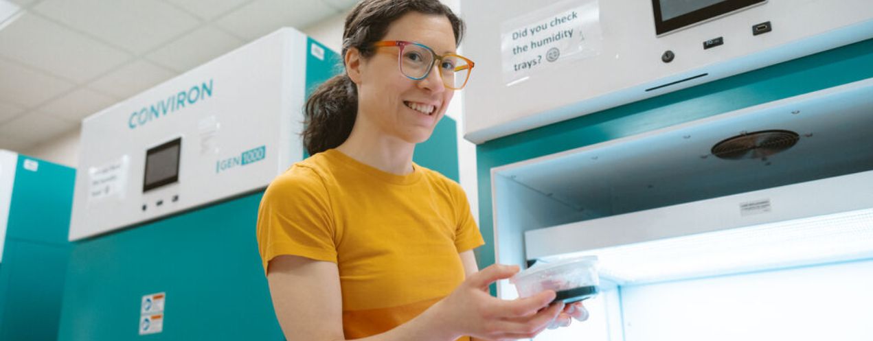 A woman researcher holding a petri dish in front of a growing chamber.