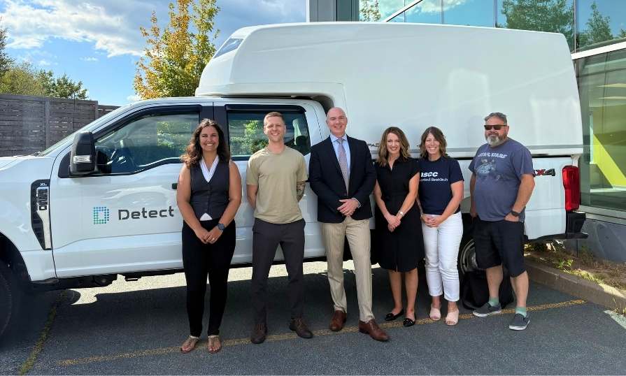 Six business professionals smiling in front of a Detect-branded truck.