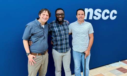 Three men with their arms around one another smiling in front of an NSCC banner.