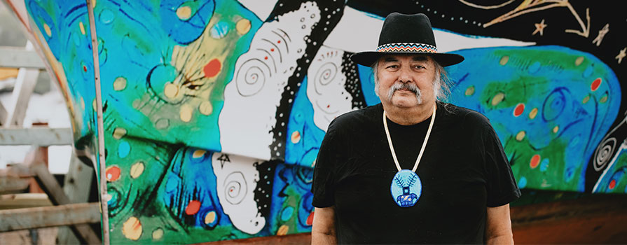 Mi'kmaw artist, Alan Syliboy, stands in front of the Alutasi, a hybrid vessel wrapped in his art.