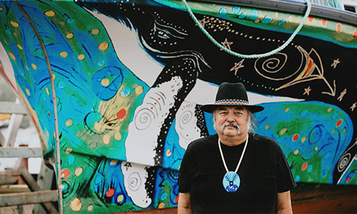 Mi'kmaw artist, Alan Syliboy, stands in front of the Alutasi, a hybrid vessel wrapped in his art.