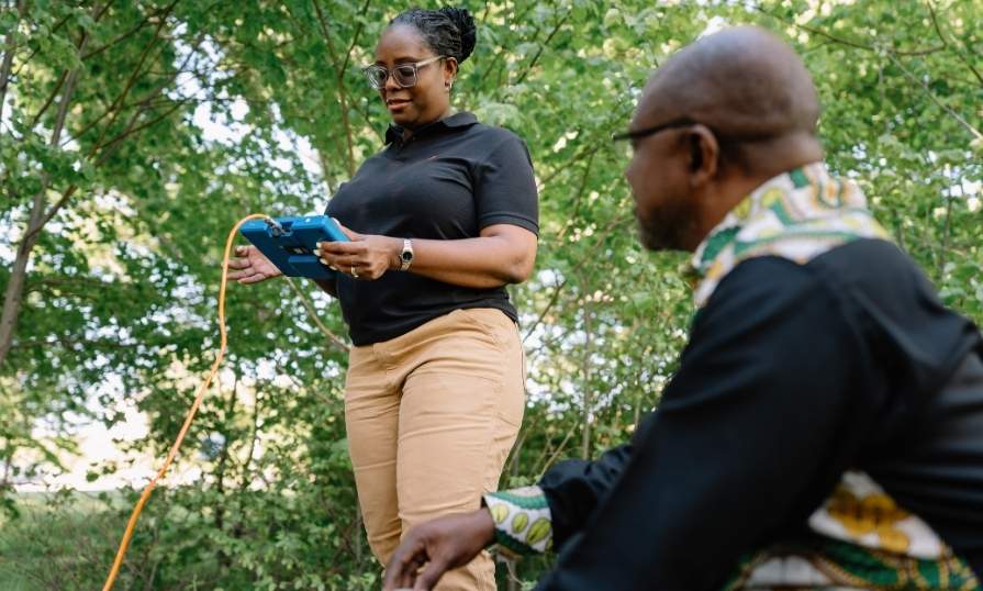 Two people outdoors in looking at a monitor connected to the ground.