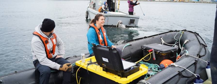 Young male and female aboard a small zodiac surrounded by research technology.