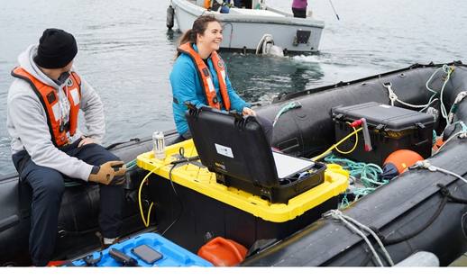 Young male and female aboard a small zodiac surrounded by research technology.