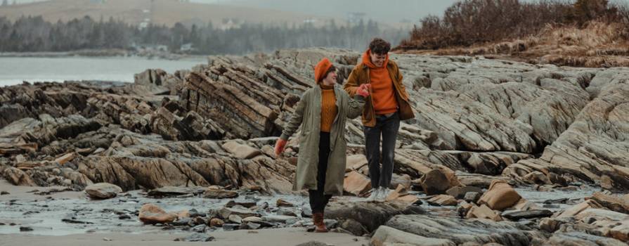 Two women holding hands walking along a rocky coastline on a foggy day. 