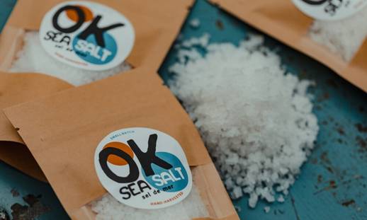 Several packages of OK Sea Salt on rustic turquoise table with a pile of salt. 