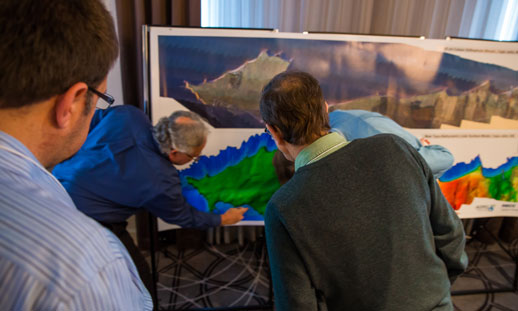 A group of men examining two large detailed maps. 