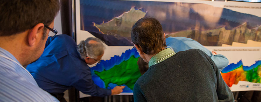 A group of men examining two large detailed maps. 