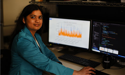 Woman researcher looking at two monitors showing complex data. 