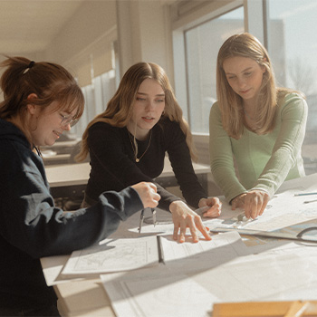 Three students of the marine navigation technology program gathered around a table working on navigation charts