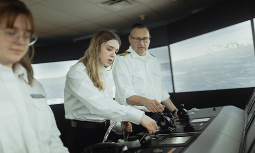 Two Marine Navigation Technology students with an instructor using controls in the bridge simulator