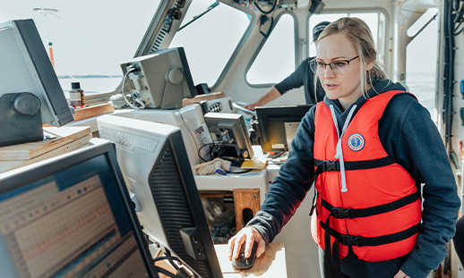 Marine Geomatics student standing on a ship while looking at a computer screen