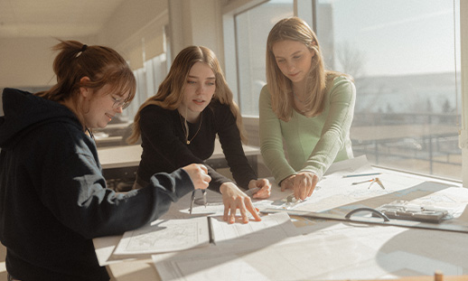 Three Marine Navigation Technology students in a classroom setting looking at navigation charts