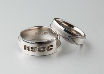 Two NSCC alumni rings stacked together, they are silver and feature the NSCC logo and a directional arrow.