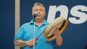 An Indigenous man standing in front of a microphone with a drum at an NSCC Convocation ceremony.