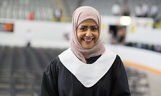 A smiling graduate is seen wearing gown and stole. 