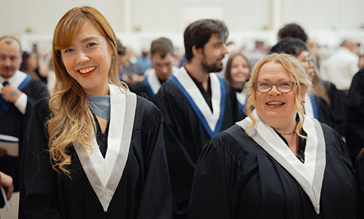 Two smiling graduates are seen wearing gowns and stoles.