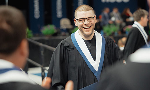 A smiling graduate in glasses is wearing a gown and stole. 