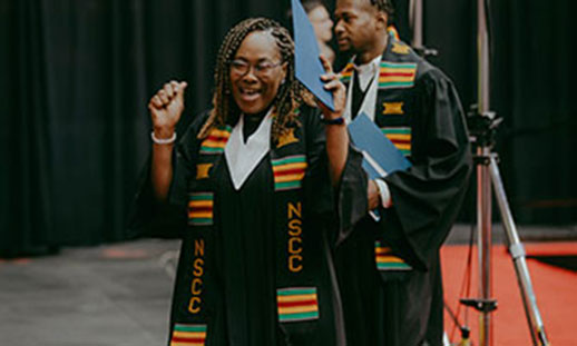 Image of an African Canadian woman wearing a Kente cloth stole is seen cheering as she receives her diploma. 