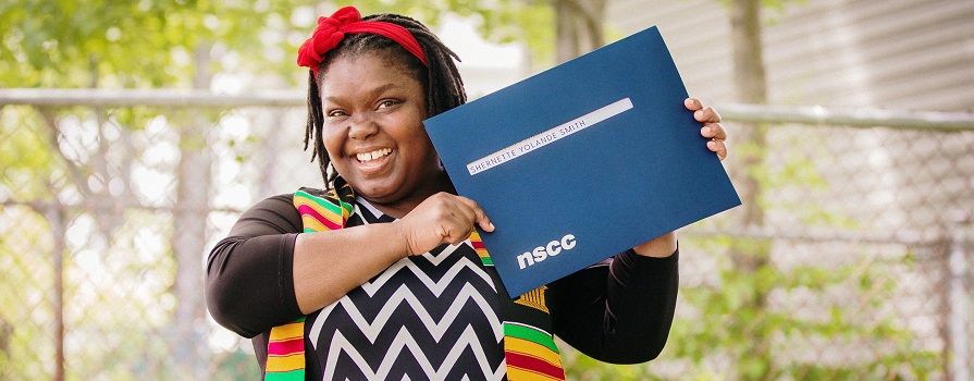 A smiling woman holding an envelope with her NSCC diploma.