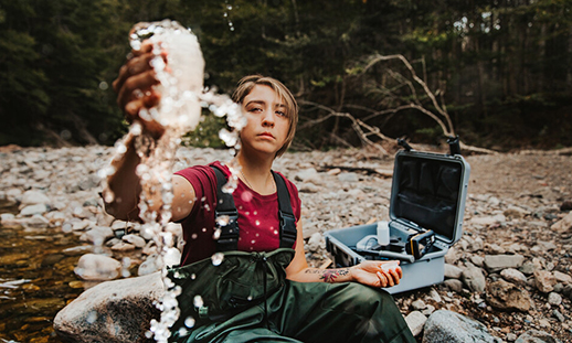 A woman laughs while working with technical equipment in a river.