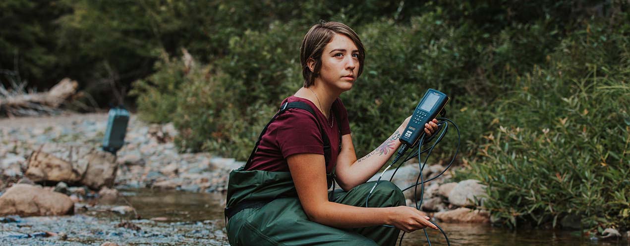 A women measures water levels in a river in the forest.