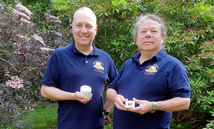 Two men stand in front of trees holding birch bark skincare products.