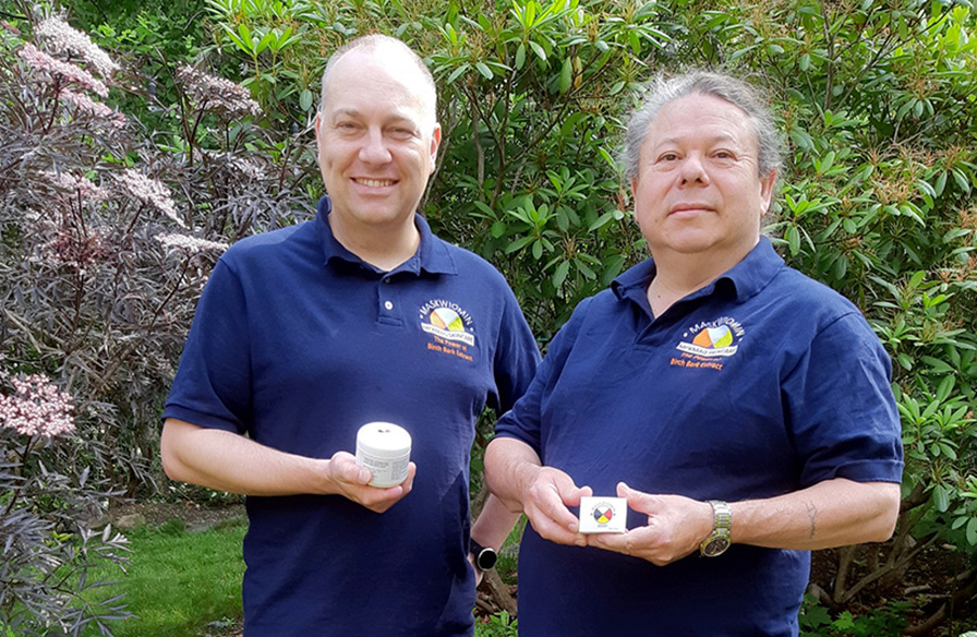 Two men stand in front of trees holding birch bark skincare products.