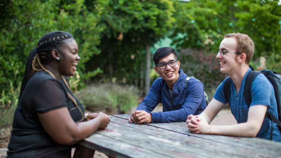 Photo of students talking and laughing outside on bench