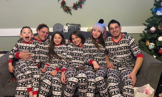 A family photo of a mom, four kids and dad sitting on their couch. They're all in matching pajamas.