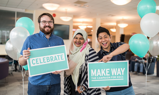 Photo of three smiling students, one holding a cyan coloured sign saying "celebrate" and another holding a cyan coloured sign saying "Make Way"