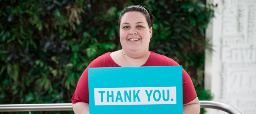 Photo of NSCC student award recipient holding aqua coloured sign saying "thank you" in white text.