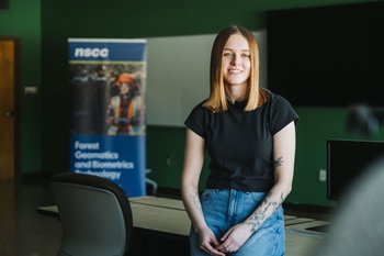 A COGS student smiles while leaning back against a table in a classroom.