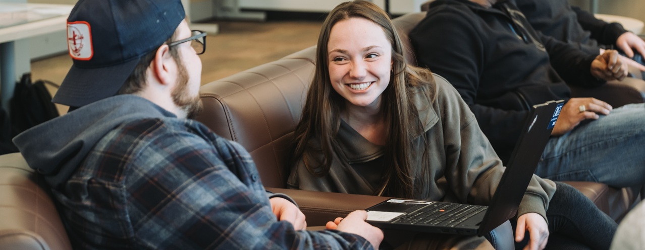 Two COGS students sit in chairs and talk while smiling.