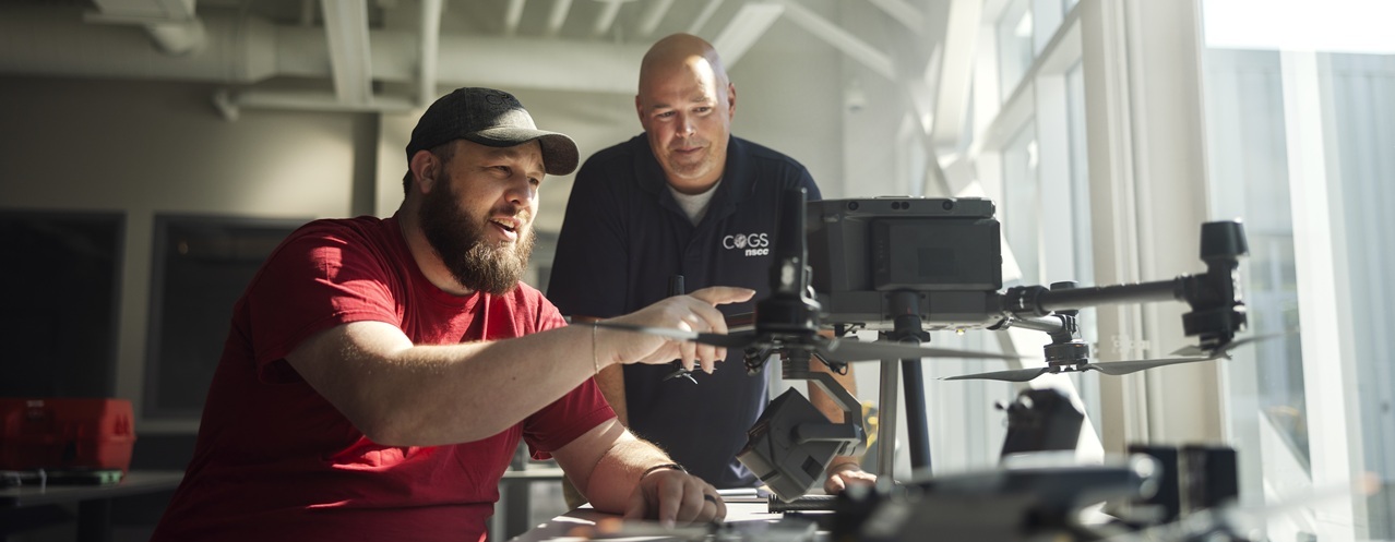A group of 5 students and instructors gather in a classroom to learn about drones.
