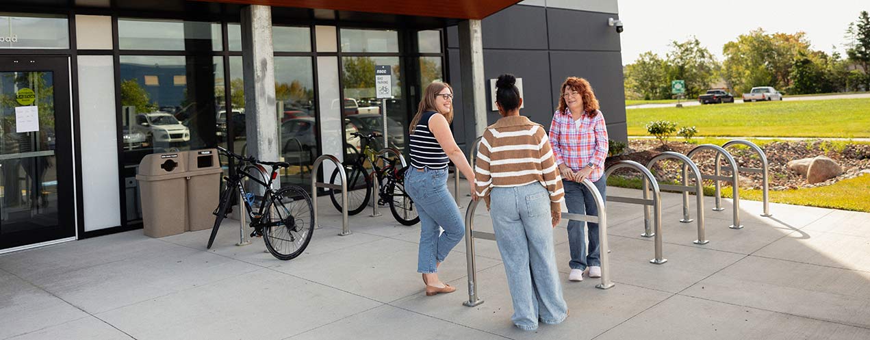 Three people stand in front of an NSCC student housing building on a sunny day.
