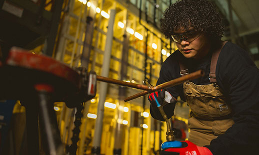 A plumbing apprentice in a dark lab learning how to sodder. 