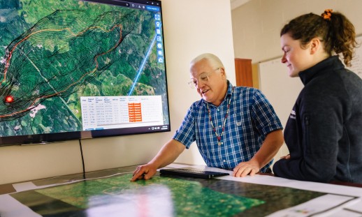 Two researchers looking at fire predictive software on a large monitor.